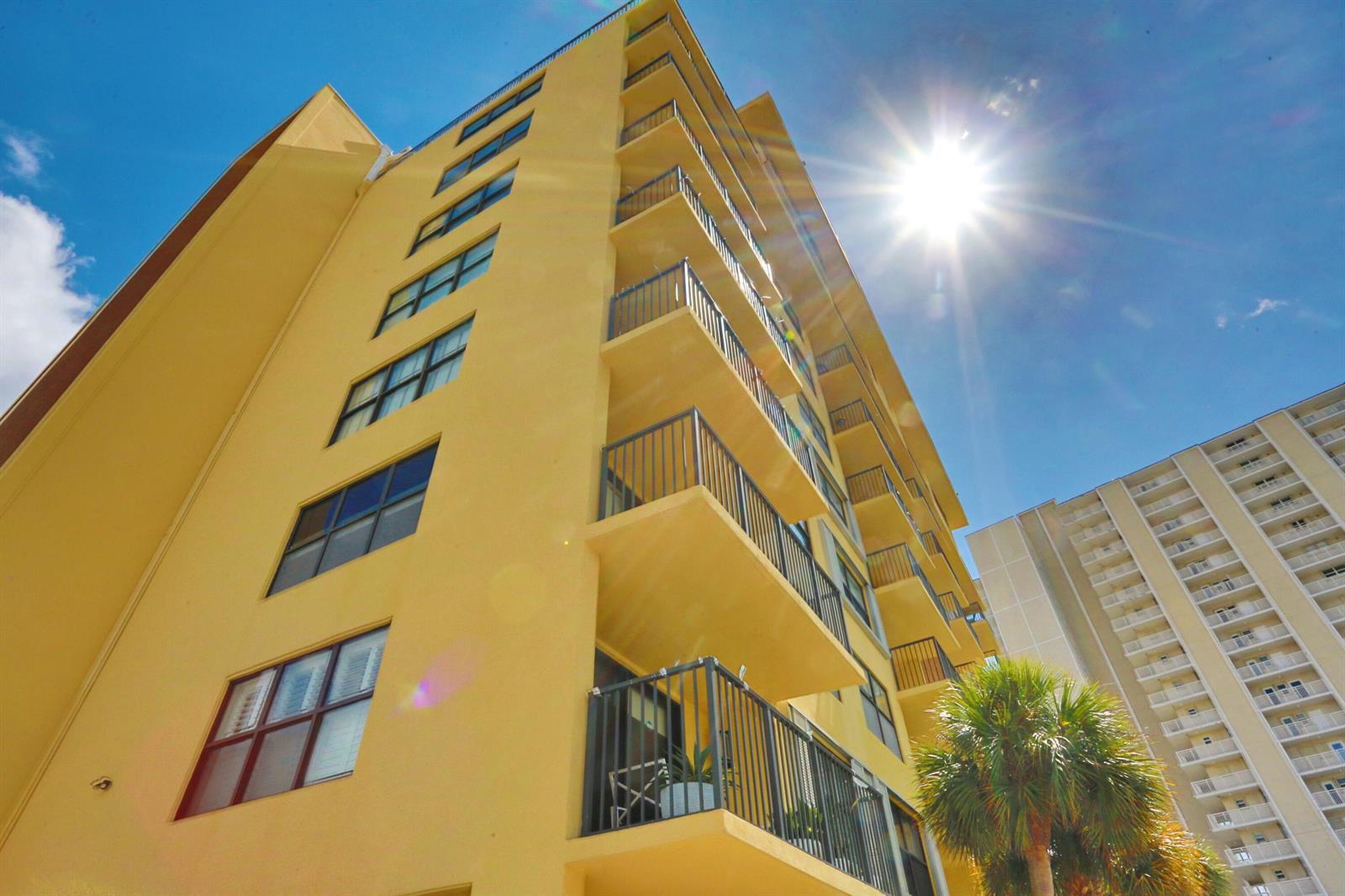 A low-angle view of a yellow high-rise building with balconies under a bright sun — 801 N Ocean Boulevard # 803, Pompano Beach FL 33062, POMPANO BEACH, FL