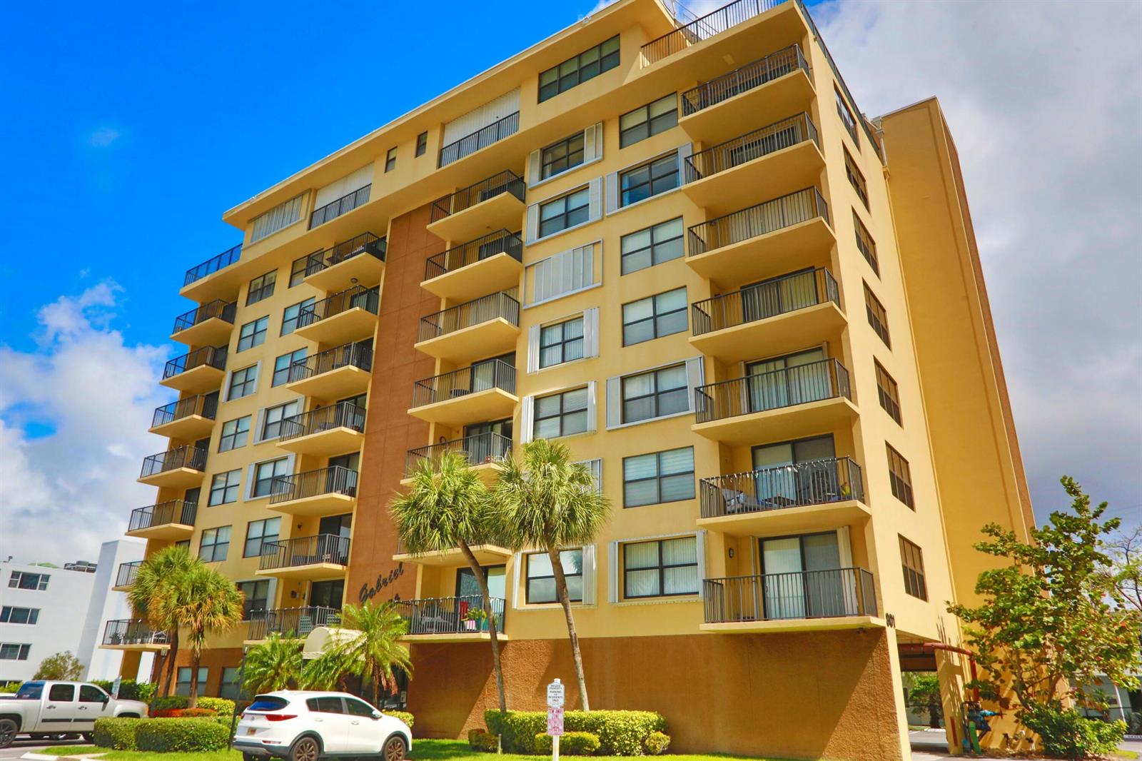 A multi-story tan apartment building features balconies and a parking area in front — 801 N Ocean Boulevard # 803, Pompano Beach FL 33062, POMPANO BEACH, FL