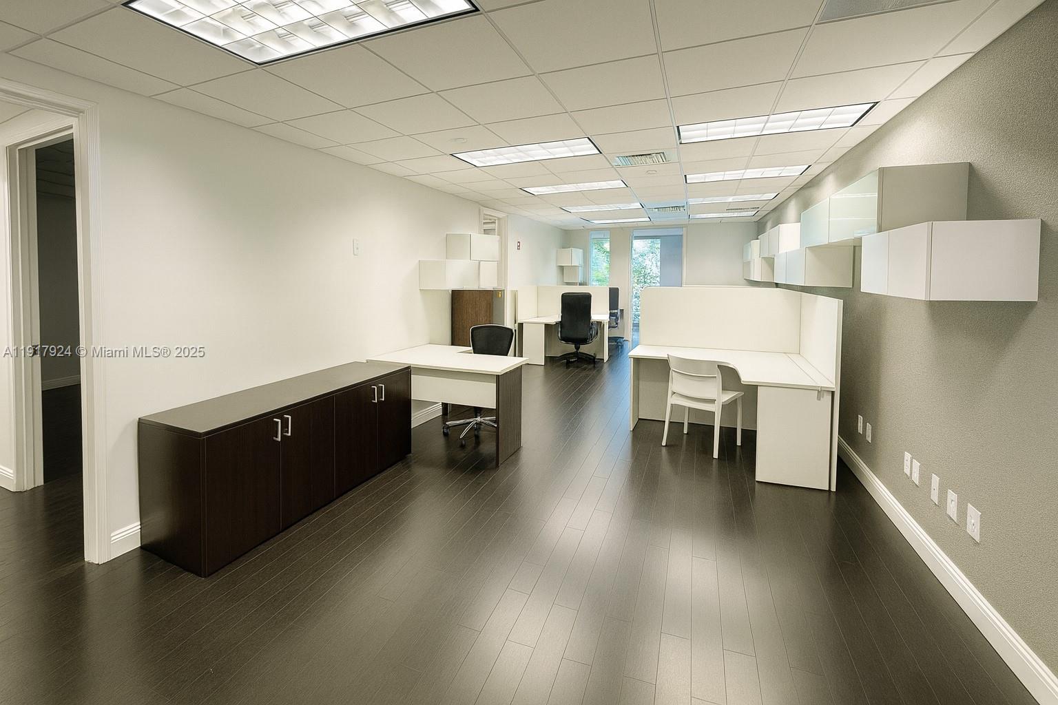 A modern office space features dark wood flooring, white desks, and wall-mounted storage cabinets — 1000 5th St # 303, Miami Beach FL 33139, MIAMI BEACH, FL