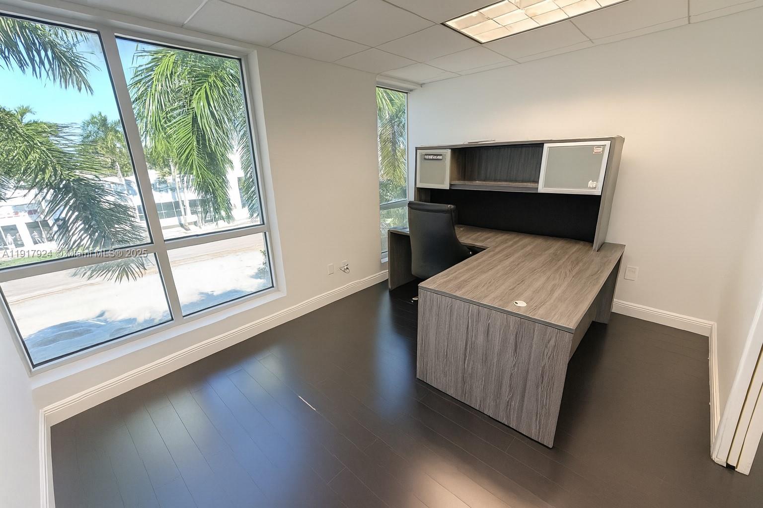 An office with a wood-grain desk, dark flooring, and large windows overlooking palm trees — 1000 5th St # 303, Miami Beach FL 33139, MIAMI BEACH, FL