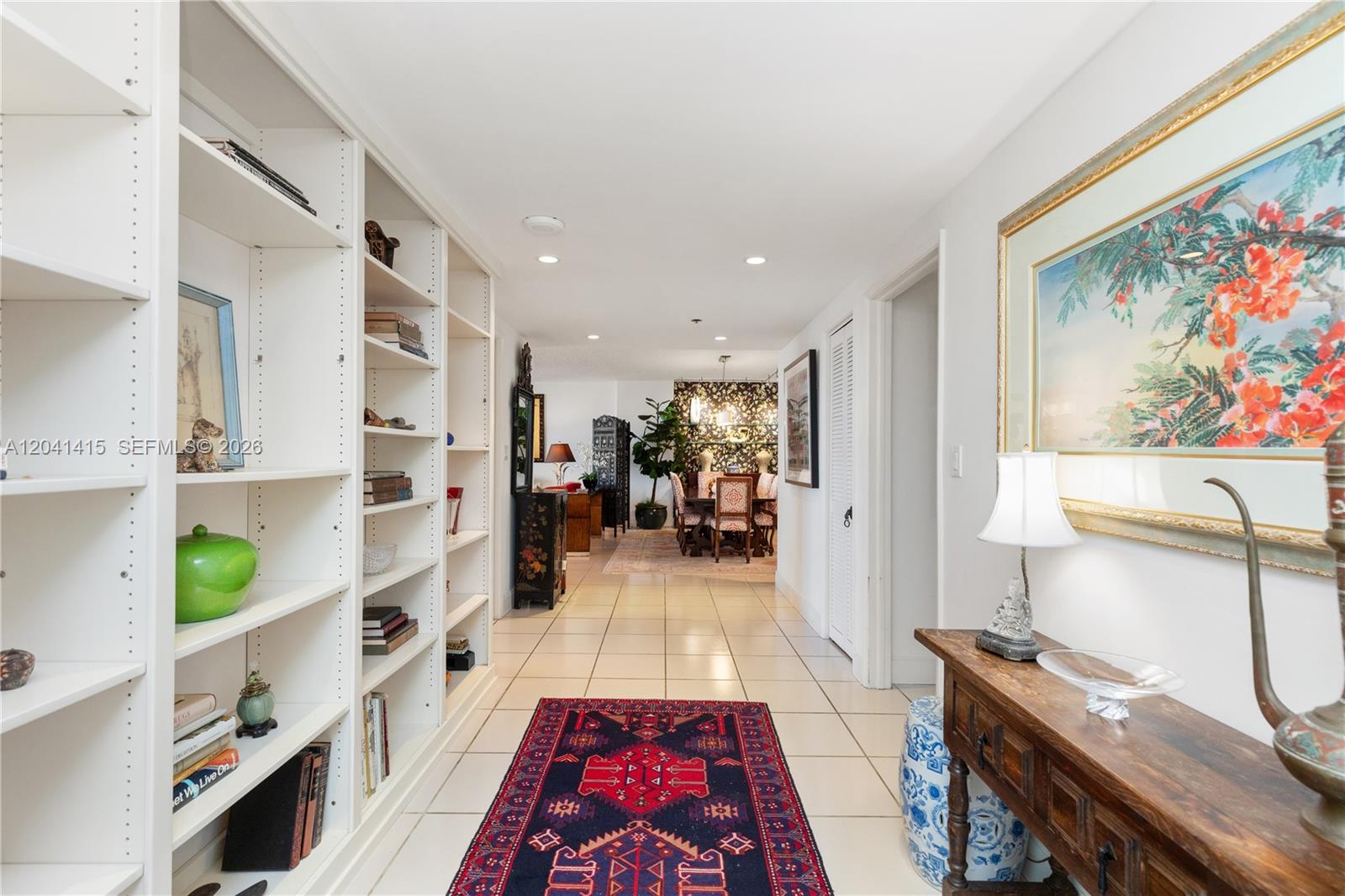 A hallway with white built-in bookshelves, tiled floors, a patterned rug, and a dining area — 1581 Brickell Ave # 903, Miami FL 33129, MIAMI, FL
