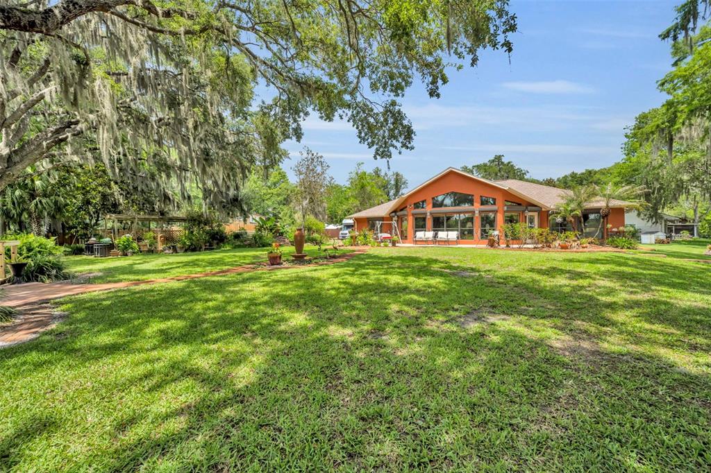A large orange house with a patio sits behind a wide, grassy lawn under trees — 4885 CR 307, LAKE PANASOFFKEE, FL