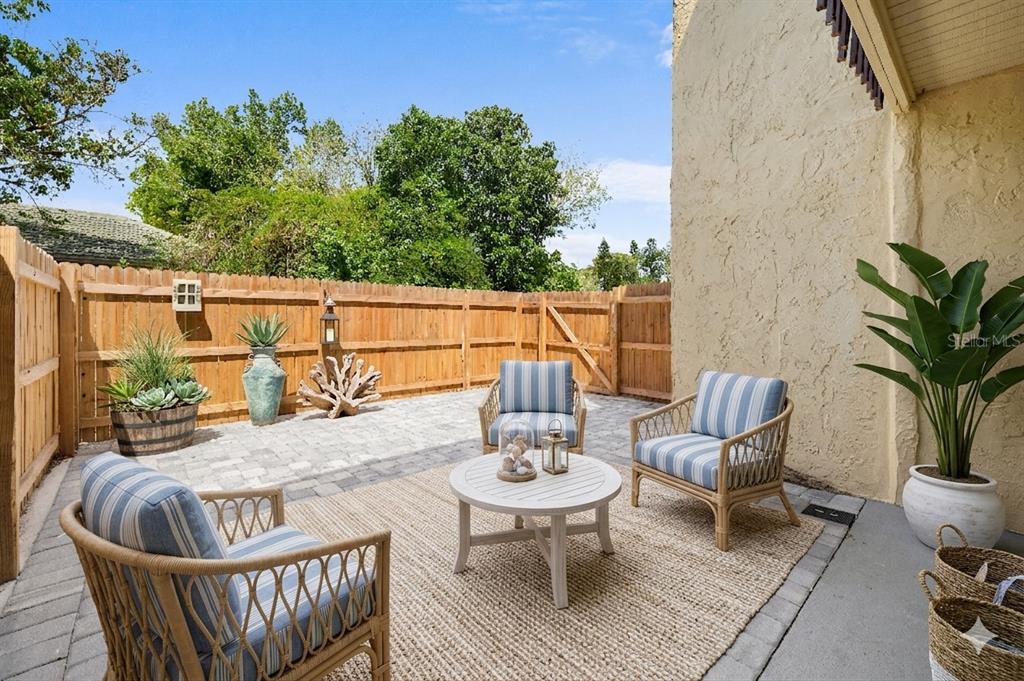 A patio features three striped chairs, a round table, and potted plants against a fence — 3411 CLARK ROAD UNIT 112, SARASOTA, FL