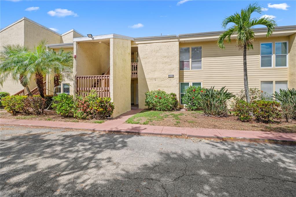 A two-story apartment building exterior with beige stucco, wood siding, and a palm tree — 3411 CLARK ROAD UNIT 112, SARASOTA, FL
