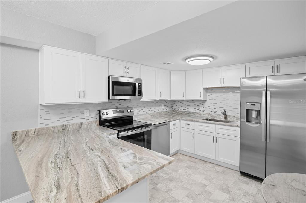 A kitchen features white cabinets, stainless steel appliances, and patterned granite countertops — 3411 CLARK ROAD UNIT 112, SARASOTA, FL