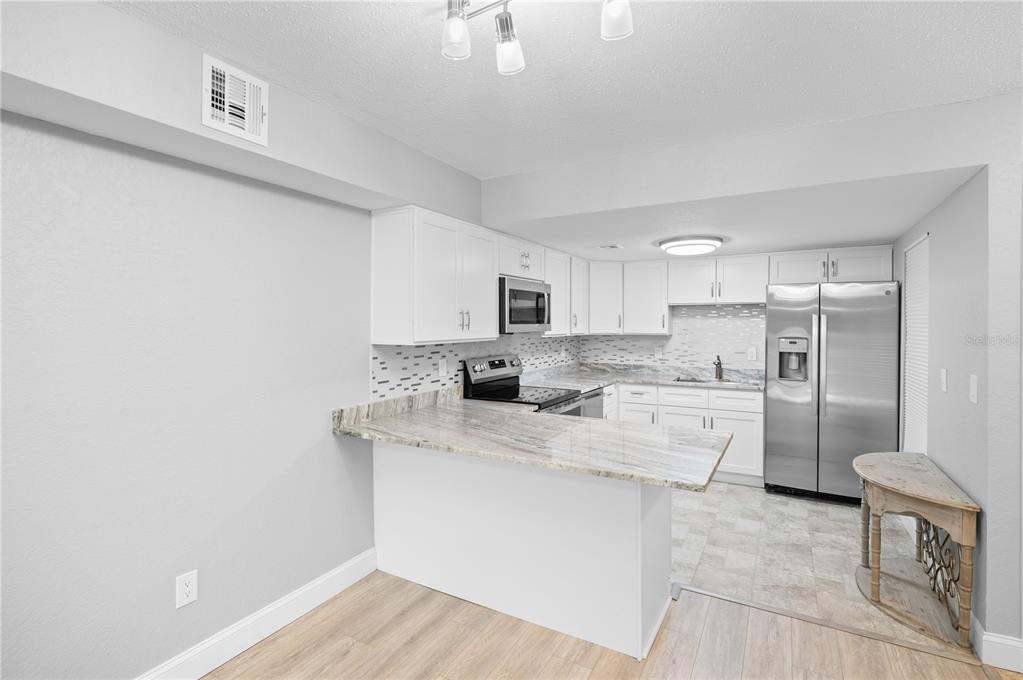A kitchen features white cabinets, granite countertops, stainless steel appliances, and a breakfast bar — 3411 CLARK ROAD UNIT 112, SARASOTA, FL