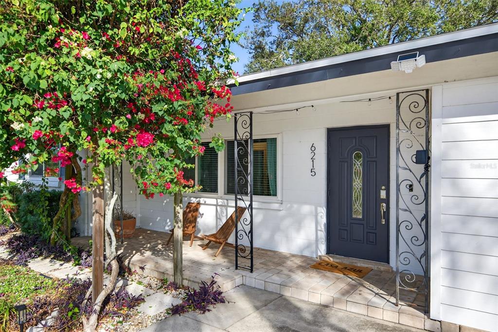 A white house exterior features a dark gray front door, decorative metal columns, and bougainvillea — 6215 RODGERS AVENUE, SARASOTA, FL