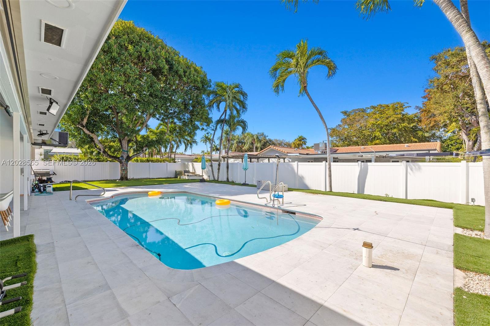 A backyard features a rectangular swimming pool surrounded by light-colored pavers and a white fence — 3460 N 46th Ave, Hollywood FL 33021, HOLLYWOOD, FL