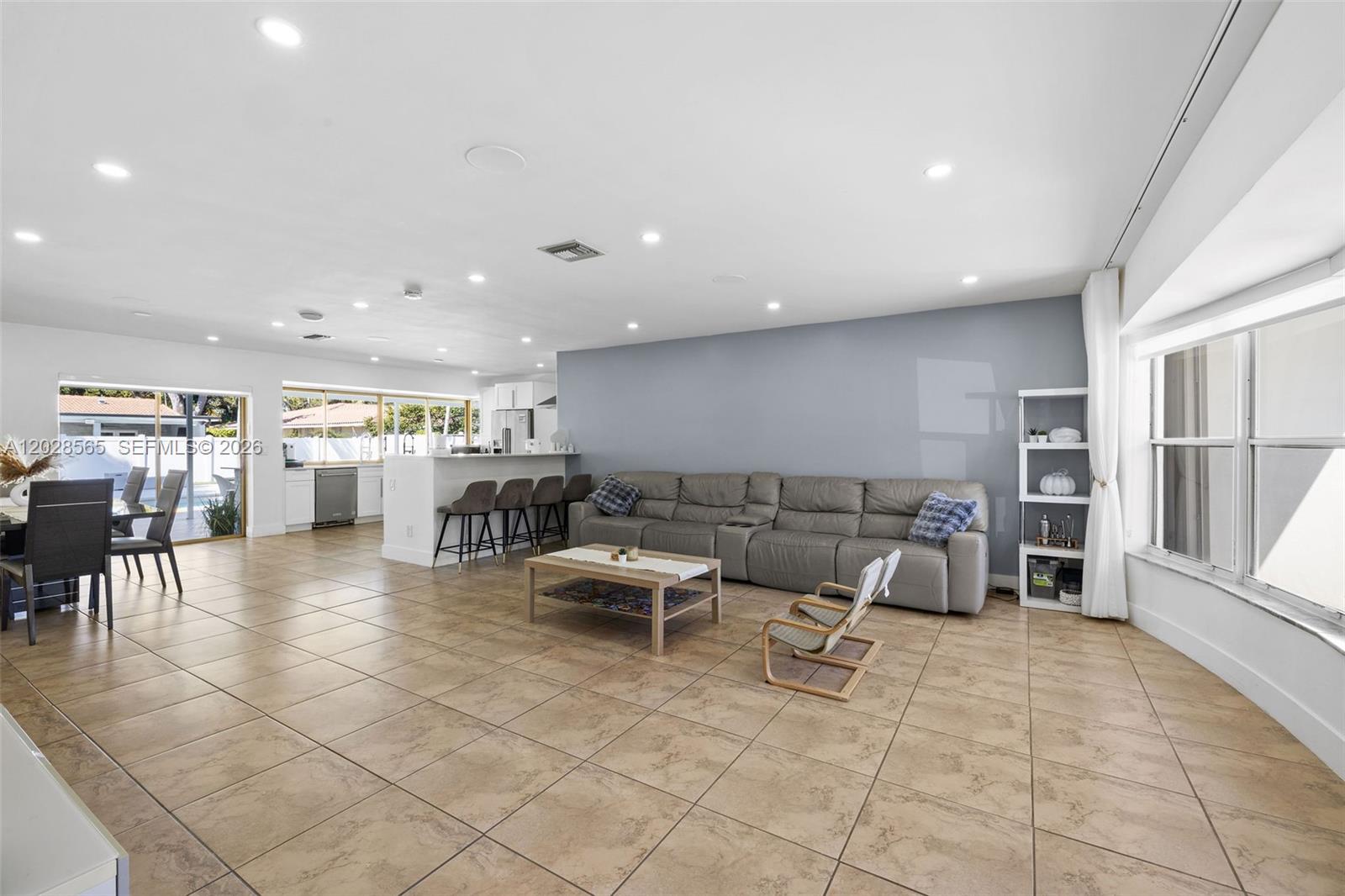 A spacious open-concept living room features tile flooring, a grey sectional sofa, and a kitchen — 3460 N 46th Ave, Hollywood FL 33021, HOLLYWOOD, FL