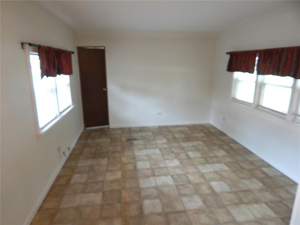 An empty room features tiled flooring, white walls, and two windows with red valances — 19 ANCHOR INN ROAD, LAKE WALES, FL