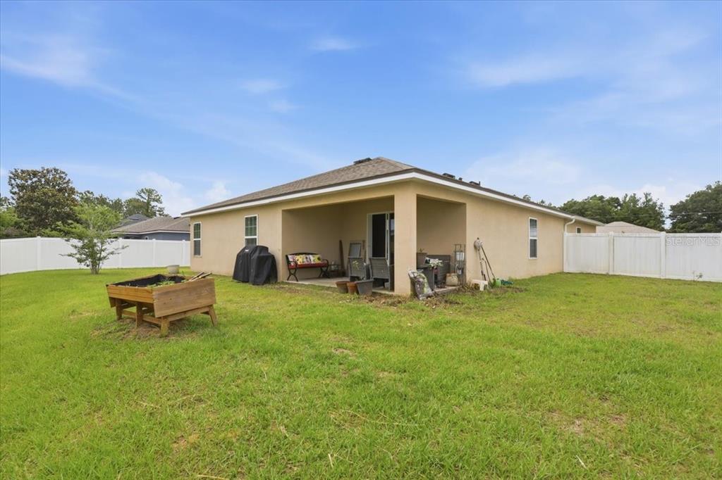 The backyard of a house features a covered patio, a wooden planter, and white fencing — 24 BUD FIELD DRIVE, PALM COAST, FL