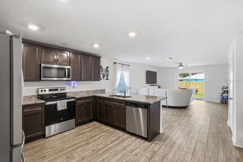 A kitchen with dark wood cabinets and granite countertops opens into a living area — 24 BUD FIELD DRIVE, PALM COAST, FL