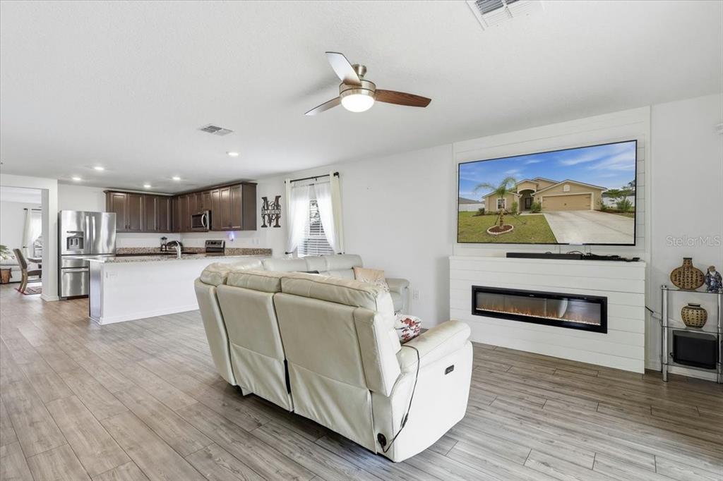 A living room features a white shiplap fireplace, a large television, and light wood flooring — 24 BUD FIELD DRIVE, PALM COAST, FL