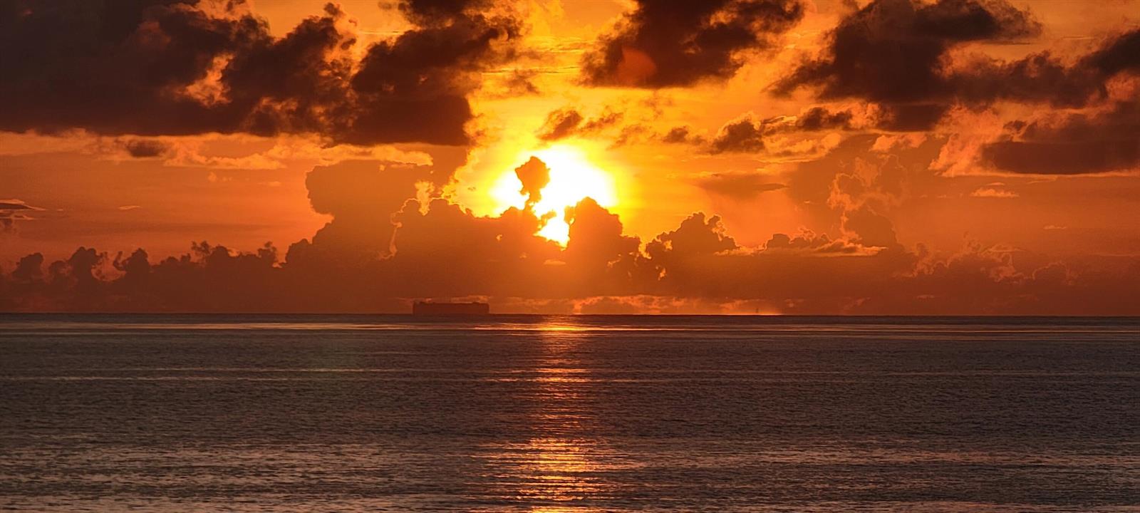 A vibrant orange sunset glows over the ocean horizon with clouds and a distant ship — 5510 N Ocean Drive # 2c, Singer Island FL 33404, SINGER ISLAND, FL