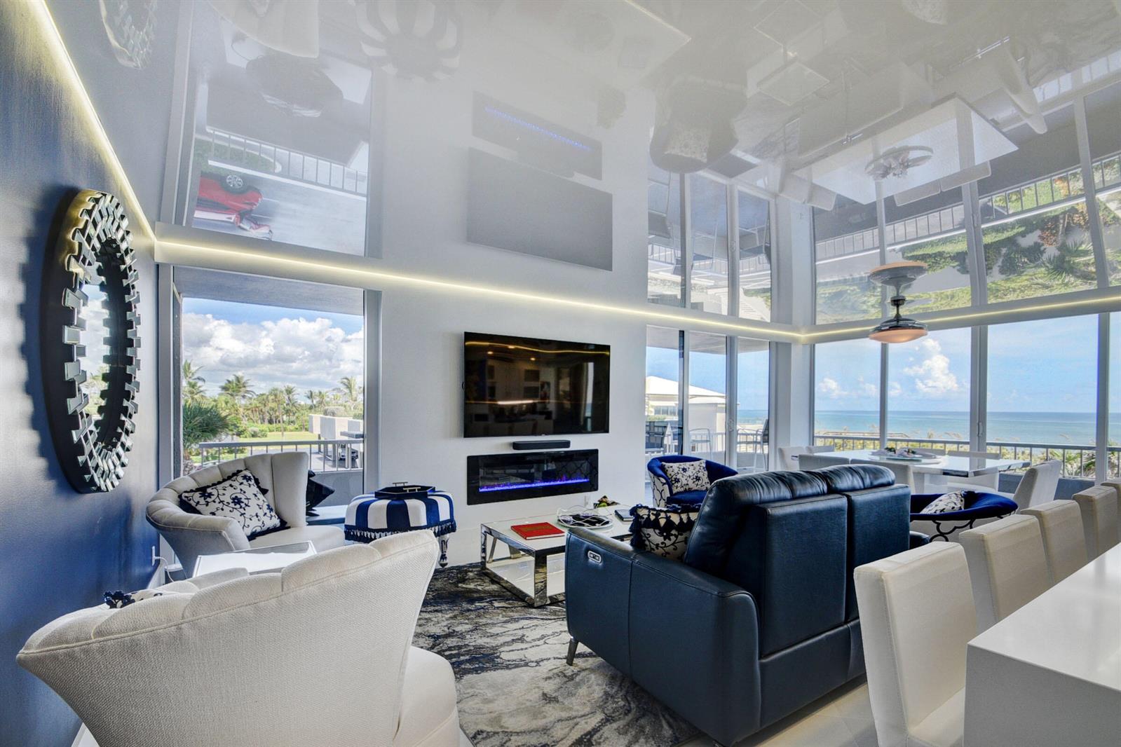 A modern living room features a high-gloss reflective ceiling, blue accent wall, and ocean views — 5510 N Ocean Drive # 2c, Singer Island FL 33404, SINGER ISLAND, FL