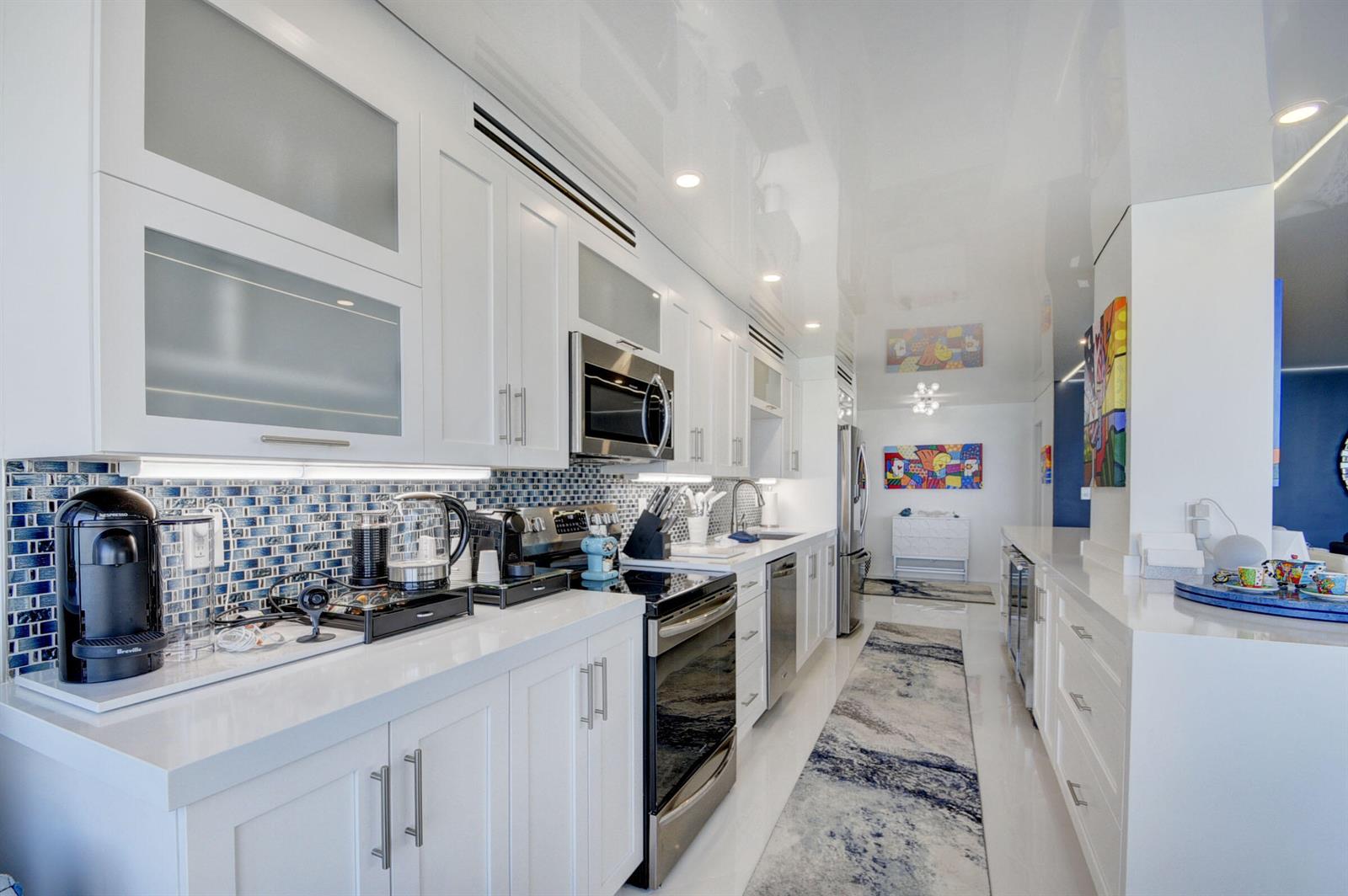 A modern white kitchen features stainless steel appliances, a blue mosaic backsplash, and glossy ceilings — 5510 N Ocean Drive # 2c, Singer Island FL 33404, SINGER ISLAND, FL