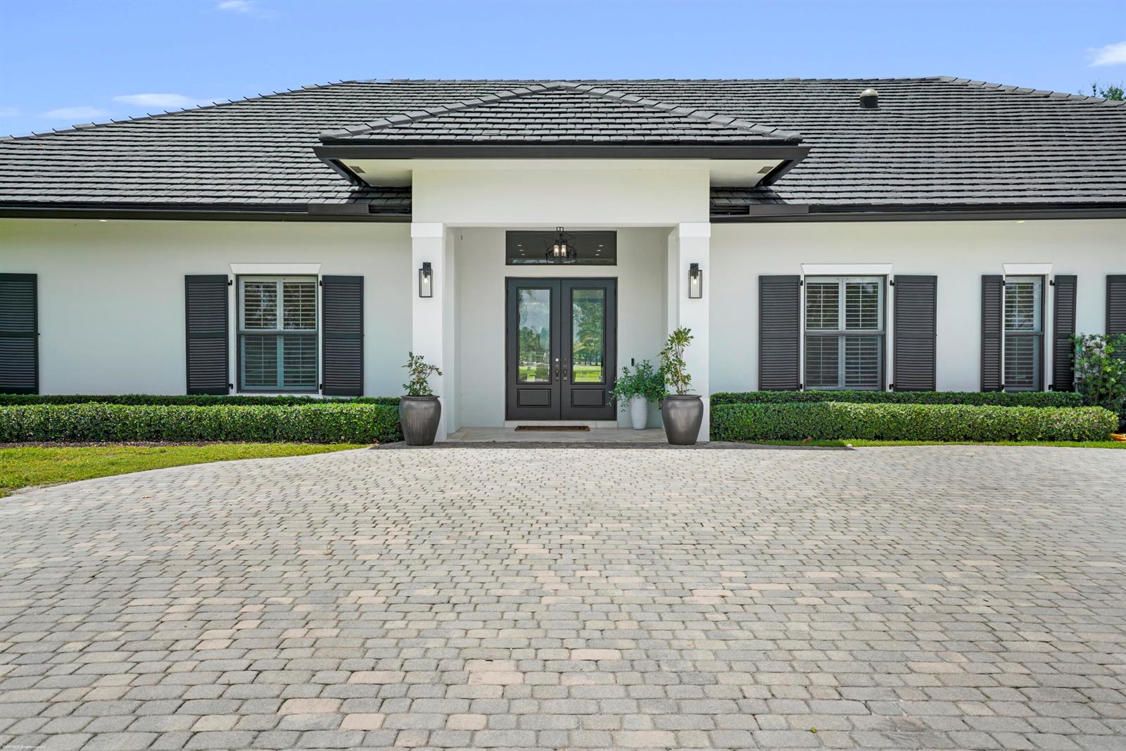 A white house with black shutters and a dark tiled roof features a paved driveway — 16451 Norris Road, Wellington FL 33470, WELLINGTON, FL