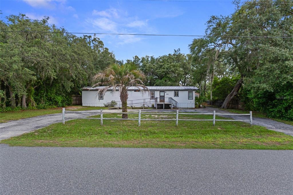 A single-story mobile home with a wheelchair ramp sits behind a wooden fence — 6463 W PARK DRIVE, HOMOSASSA, FL