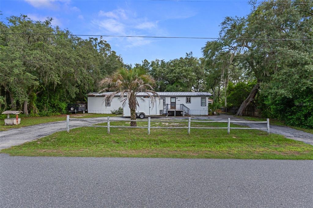 A single-story manufactured home sits behind a white fence on a wooded lot — 6463 W PARK DRIVE, HOMOSASSA, FL