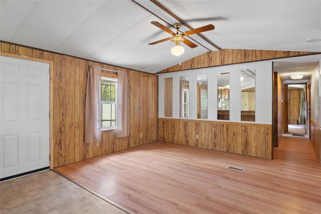 A living room with wood-paneled walls, wood-look flooring, a ceiling fan, and mirrored wall accents — 6463 W PARK DRIVE, HOMOSASSA, FL