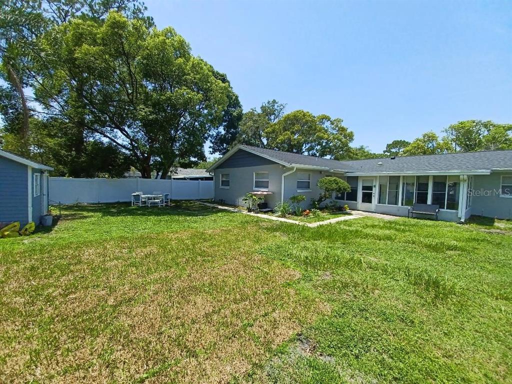 A backyard features a gray house with a sunroom, a white fence, and large trees — 1942 CONIFER COURT, WINTER PARK, FL