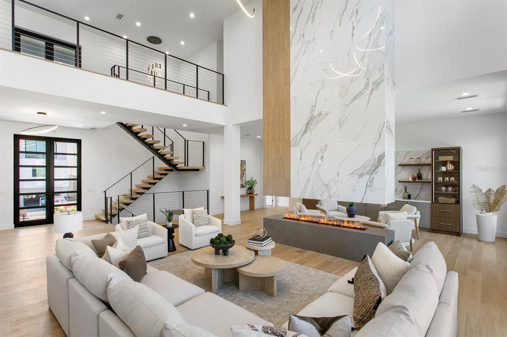 A spacious living room features a double-height ceiling, a marble fireplace, and a floating staircase — 5023 W LEONA STREET, TAMPA, FL