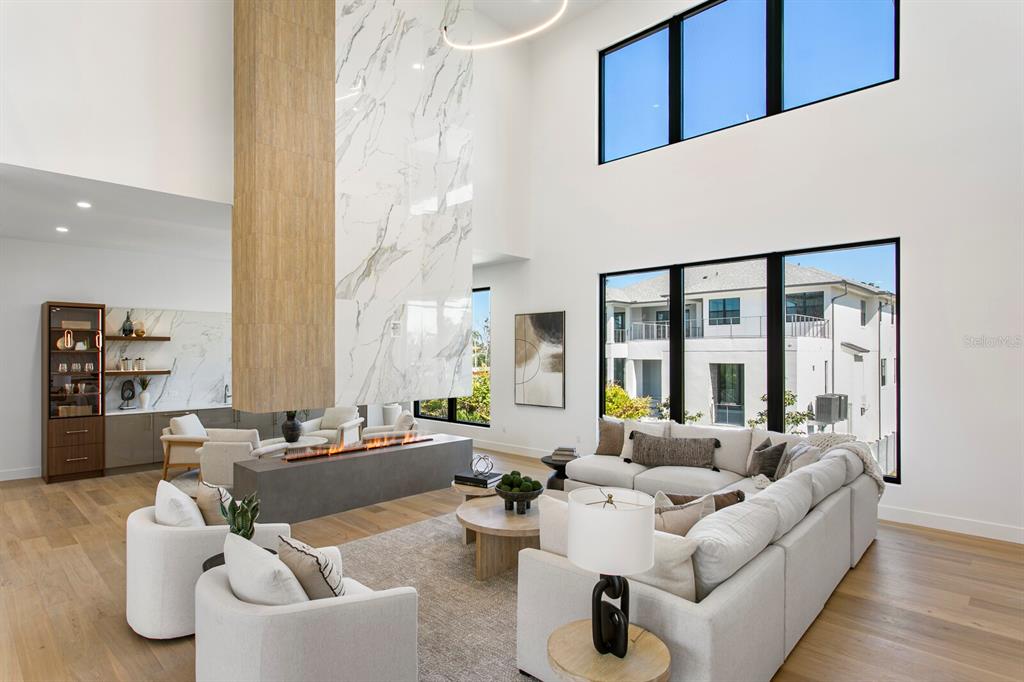 A modern living room features a double-height ceiling, a marble fireplace, and large windows — 5023 W LEONA STREET, TAMPA, FL