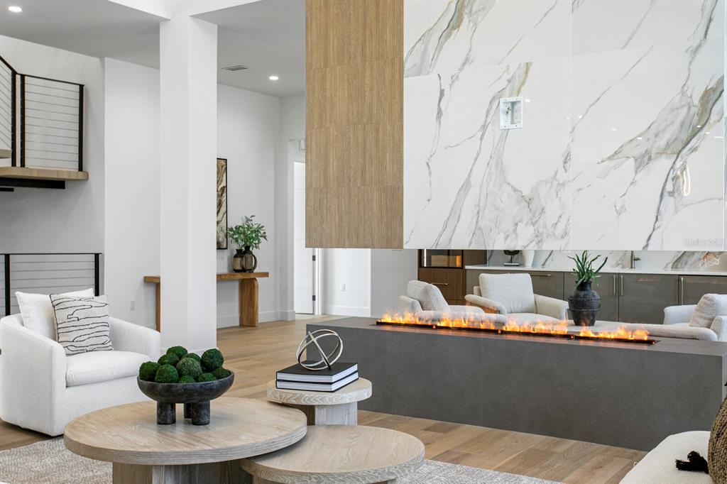 A modern living room features a linear fireplace with a marble and wood-paneled accent wall — 5023 W LEONA STREET, TAMPA, FL