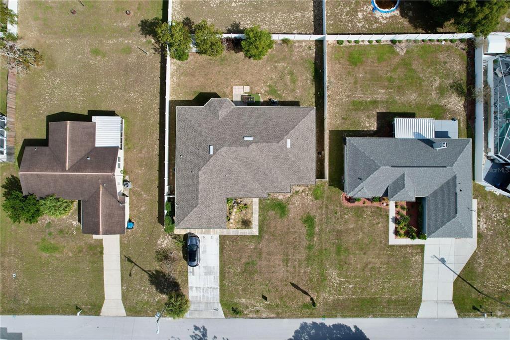 An aerial view shows three suburban houses with driveways and backyards separated by white fences — 4372 ODIN STREET, SPRING HILL, FL