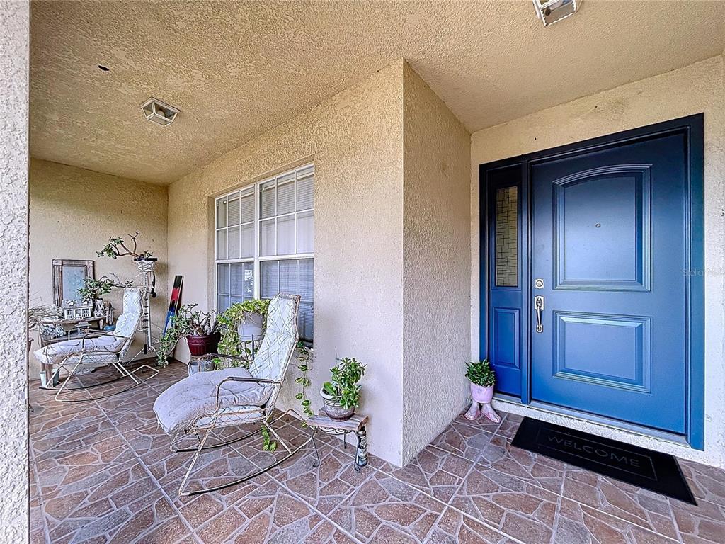 A covered front porch features a blue door, rocking chairs, and tiled flooring — 4372 ODIN STREET, SPRING HILL, FL