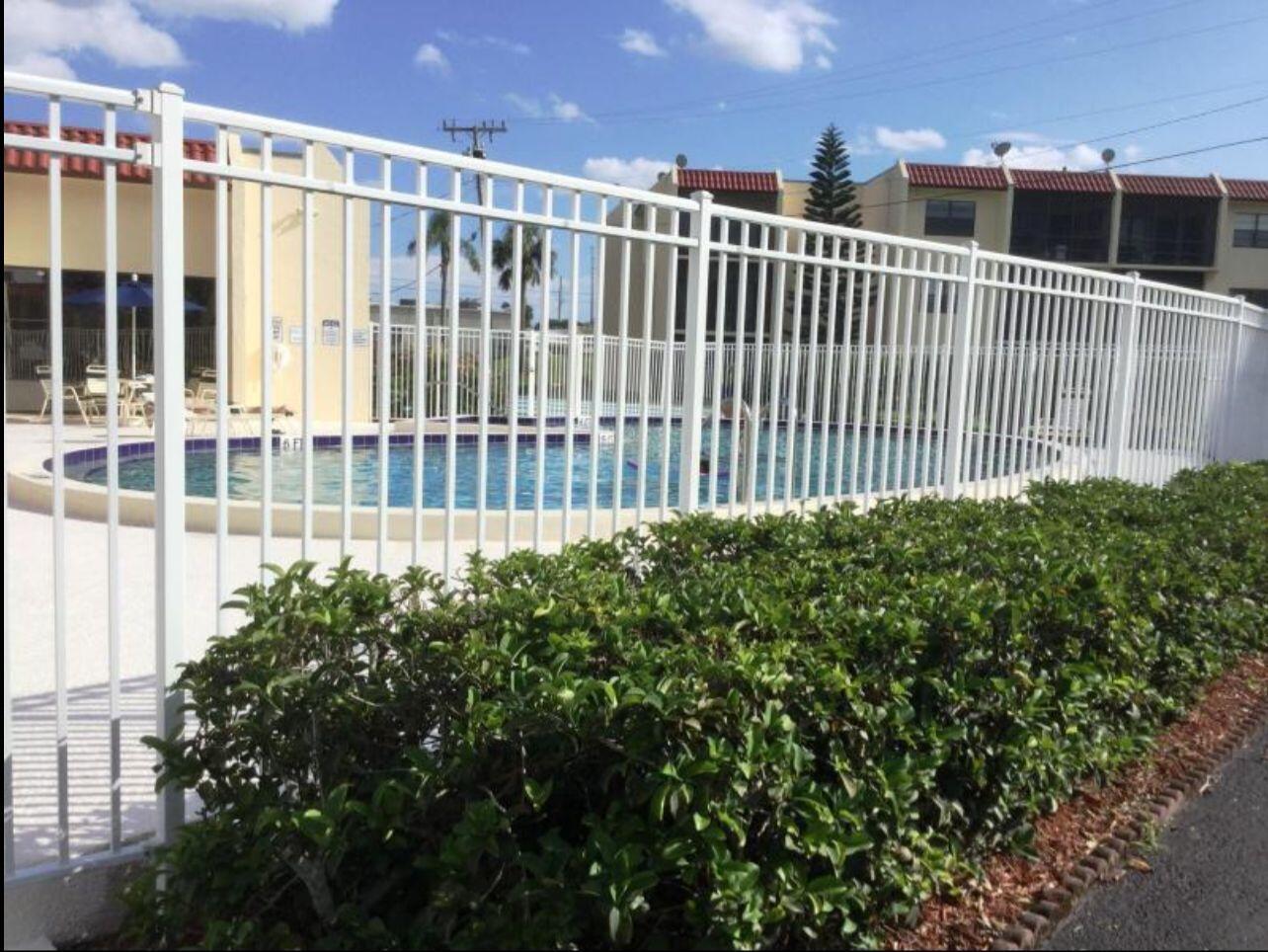 A white metal fence encloses a swimming pool area with a hedge in the foreground — 2050 Oleander Boulevard # 206, Fort Pierce FL 34950, FORT PIERCE, FL