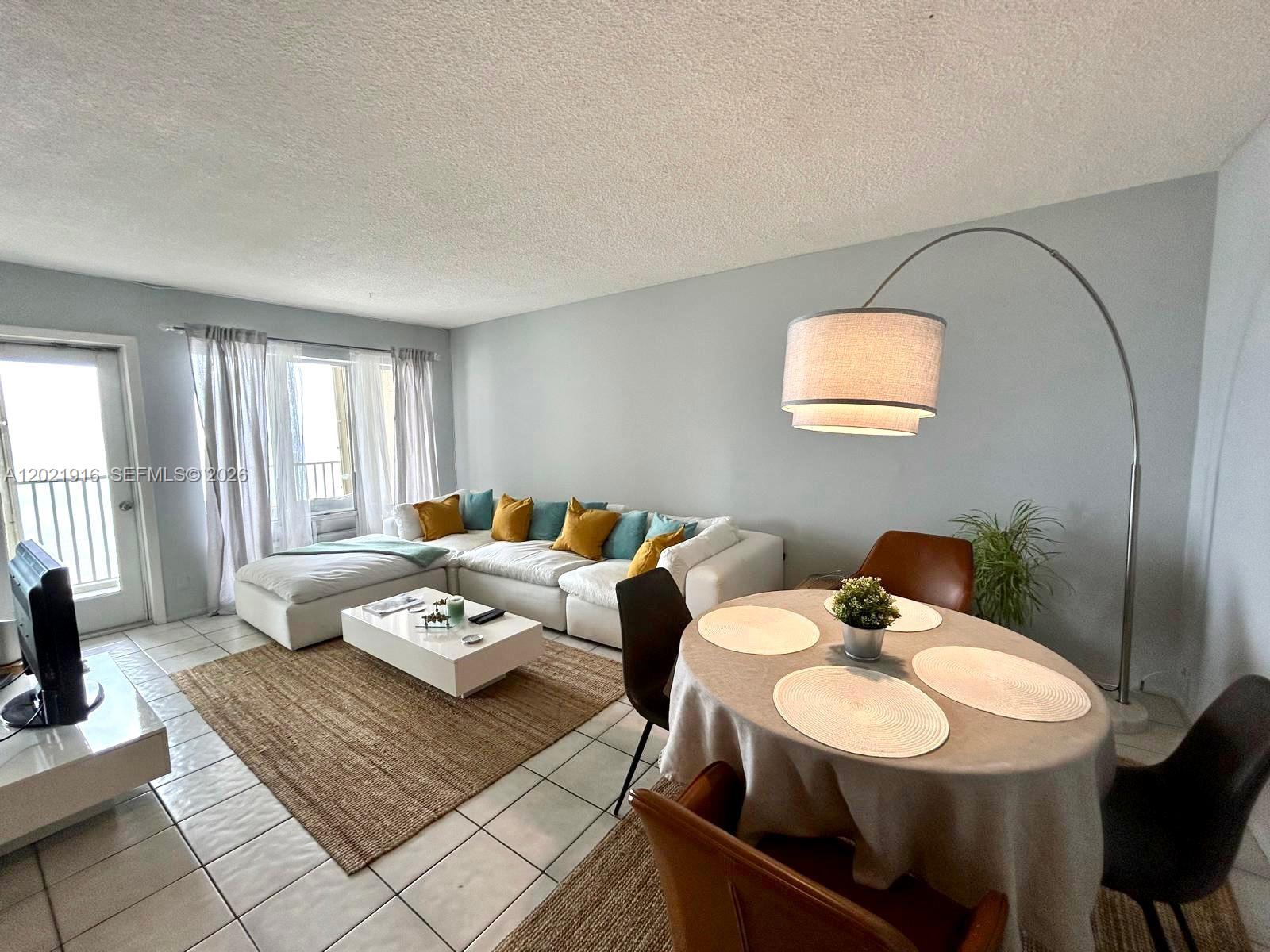 A living and dining area features a white sectional sofa, a round table, and tile flooring — 750 N Ocean Blvd # 1106, Pompano Beach FL 33062, POMPANO BEACH, FL