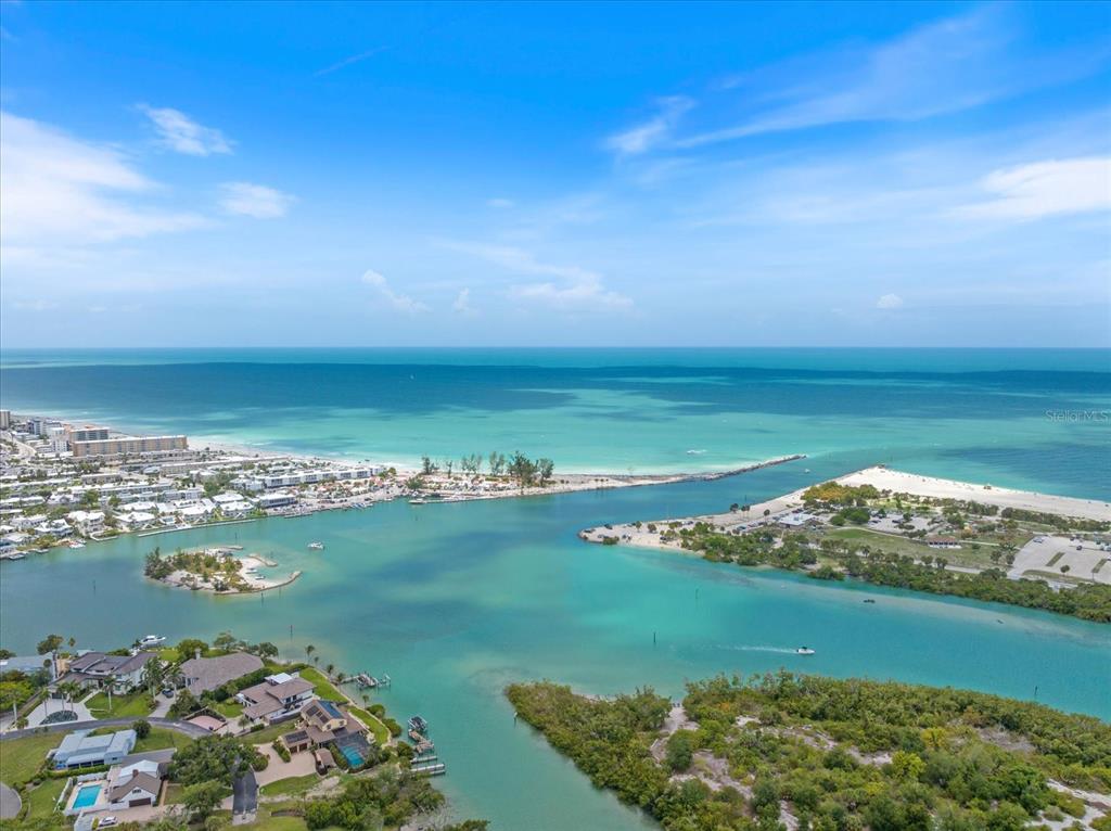 An aerial view shows a coastal inlet with turquoise water, sandy beaches, and residential homes — 1585 TARPON CENTER DRIVE UNIT 20, VENICE, FL