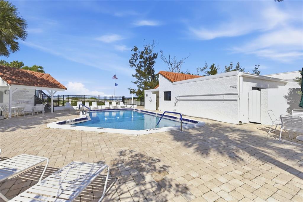 An outdoor swimming pool surrounded by a paved patio and white lounge chairs — 1585 TARPON CENTER DRIVE UNIT 20, VENICE, FL