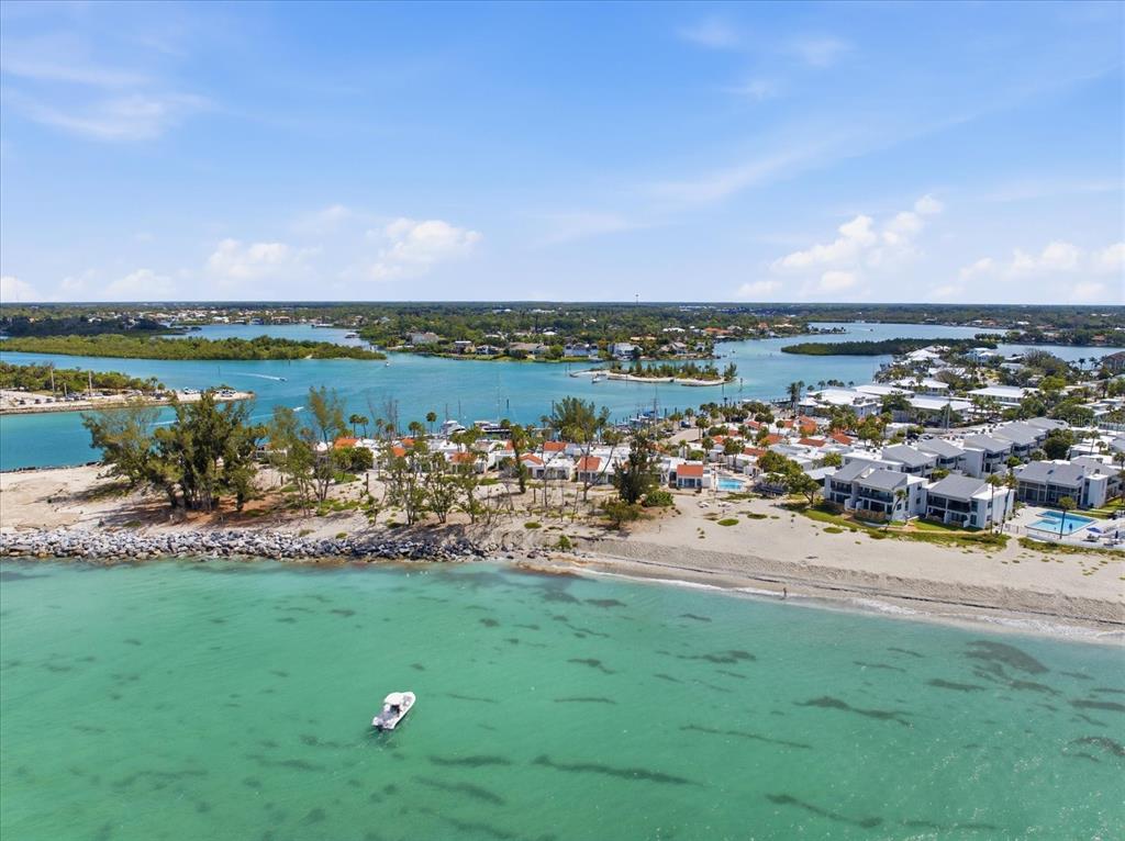 An aerial view shows a coastal resort with white buildings, a beach, and turquoise water — 1585 TARPON CENTER DRIVE UNIT 20, VENICE, FL