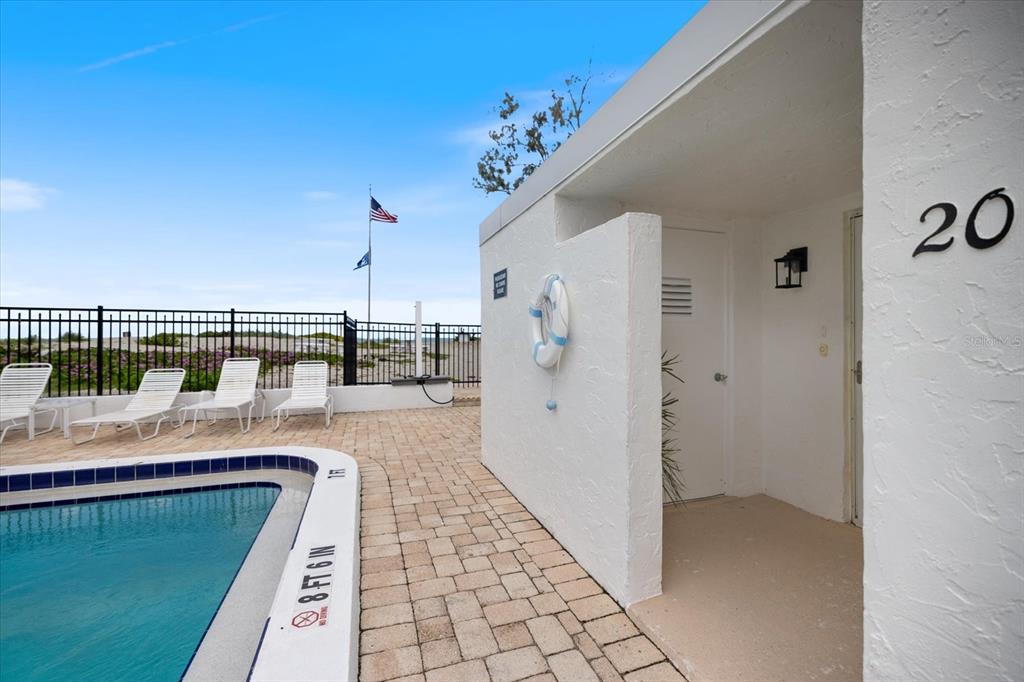 A swimming pool with lounge chairs sits beside a white building marked with the number 20 — 1585 TARPON CENTER DRIVE UNIT 20, VENICE, FL