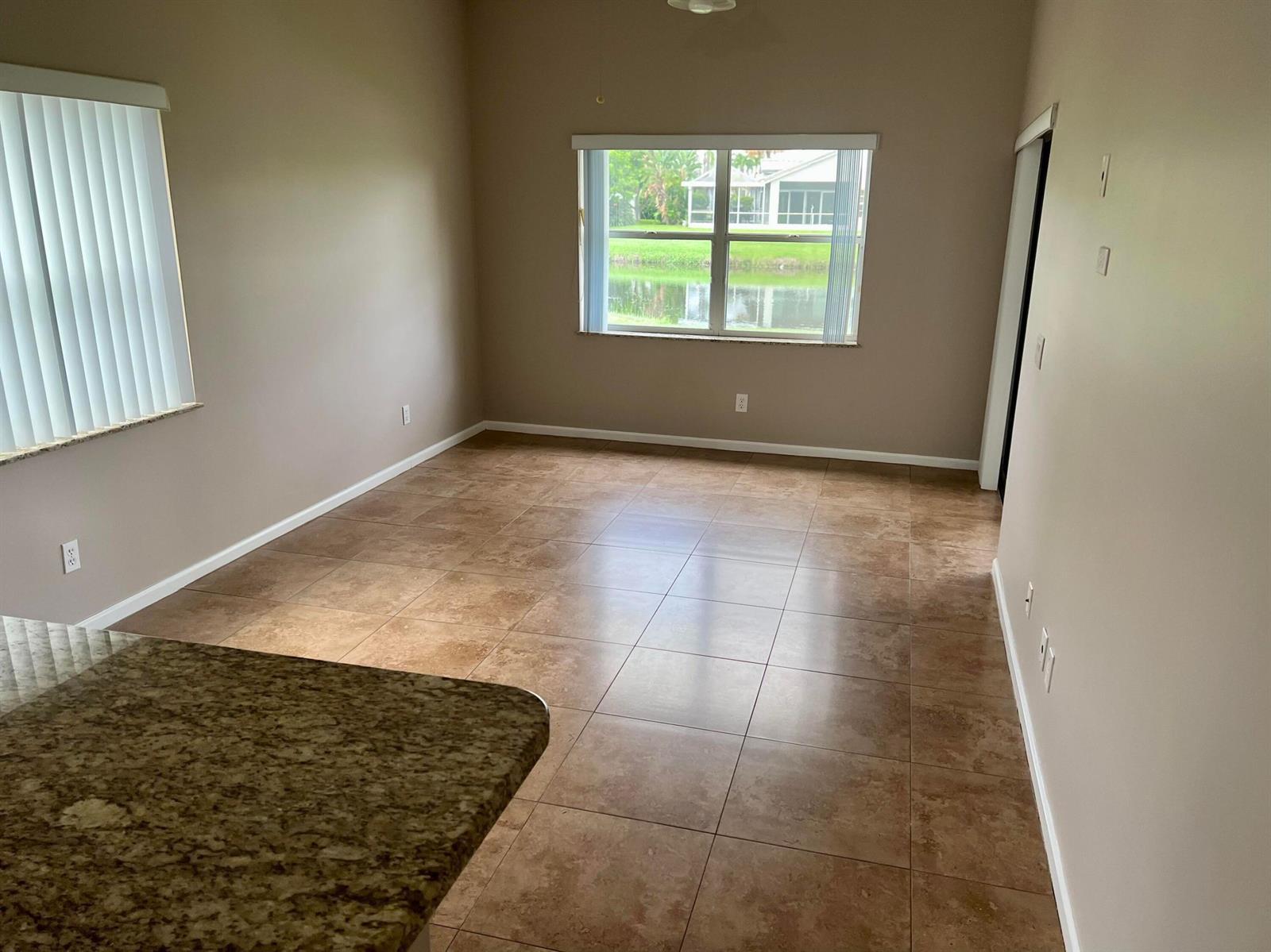 An empty room with brown tile flooring, beige walls, and a view of a lake — 6365 Lansdowne Circle, Boynton Beach FL 33472, BOYNTON BEACH, FL