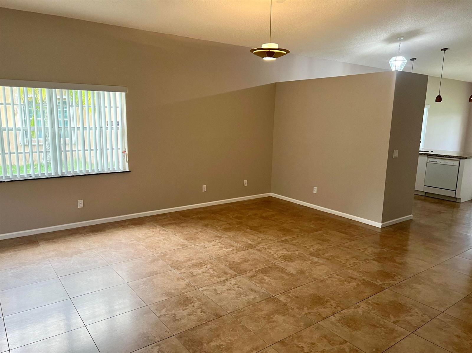 An open living area features tan tile flooring, neutral walls, and a large window — 6365 Lansdowne Circle, Boynton Beach FL 33472, BOYNTON BEACH, FL