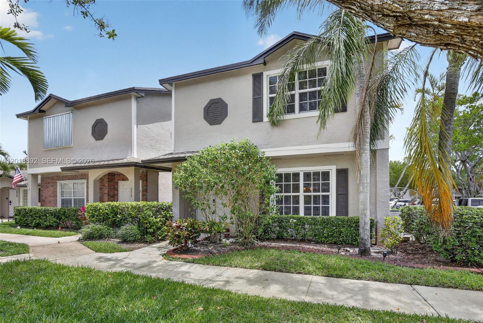 A two-story townhouse with beige stucco siding, dark shutters, and a landscaped front yard — 3815 NW 122nd Ter # 3815, Sunrise FL 33323, SUNRISE, FL