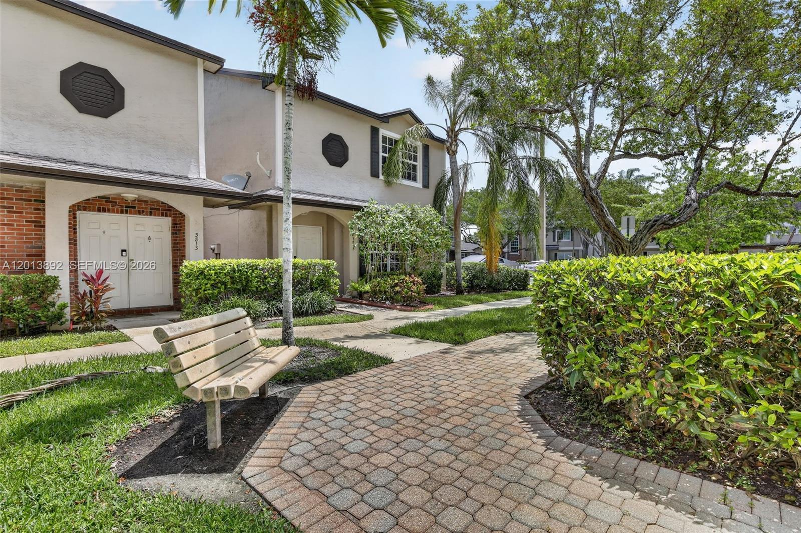 A wooden bench sits on a brick walkway in front of two-story townhouses with landscaping — 3815 NW 122nd Ter # 3815, Sunrise FL 33323, SUNRISE, FL
