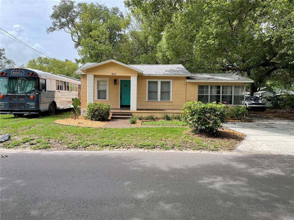 A yellow single-story house with a turquoise front door sits next to a parked bus — 1517 E ELLICOTT STREET, TAMPA, FL