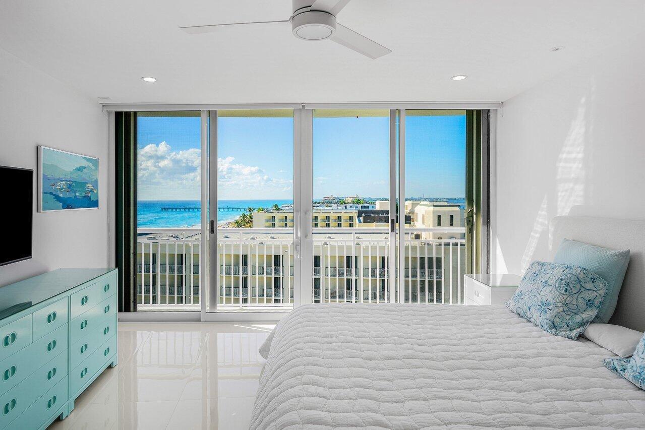 A bedroom with a light blue dresser, a white bed, and sliding doors overlooking the ocean — 2780 S Ocean Boulevard # 805, Palm Beach FL 33480, PALM BEACH, FL