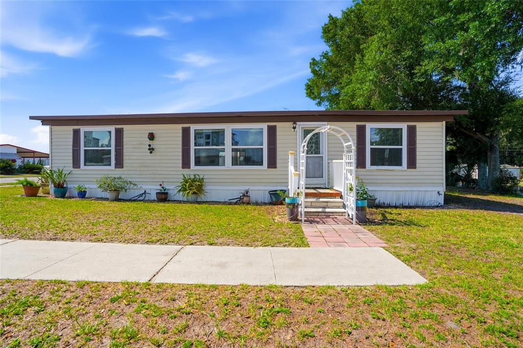 A single-story manufactured home with light siding, brown shutters, and a white garden archway — 3933 SARAH DRIVE, WESLEY CHAPEL, FL