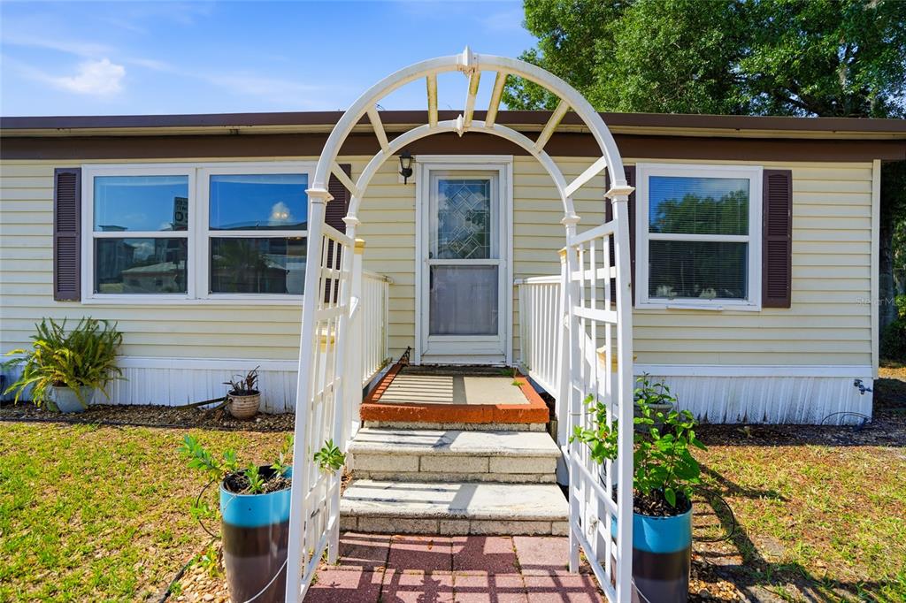 A white arched trellis stands over the front steps of a light yellow mobile home — 3933 SARAH DRIVE, WESLEY CHAPEL, FL