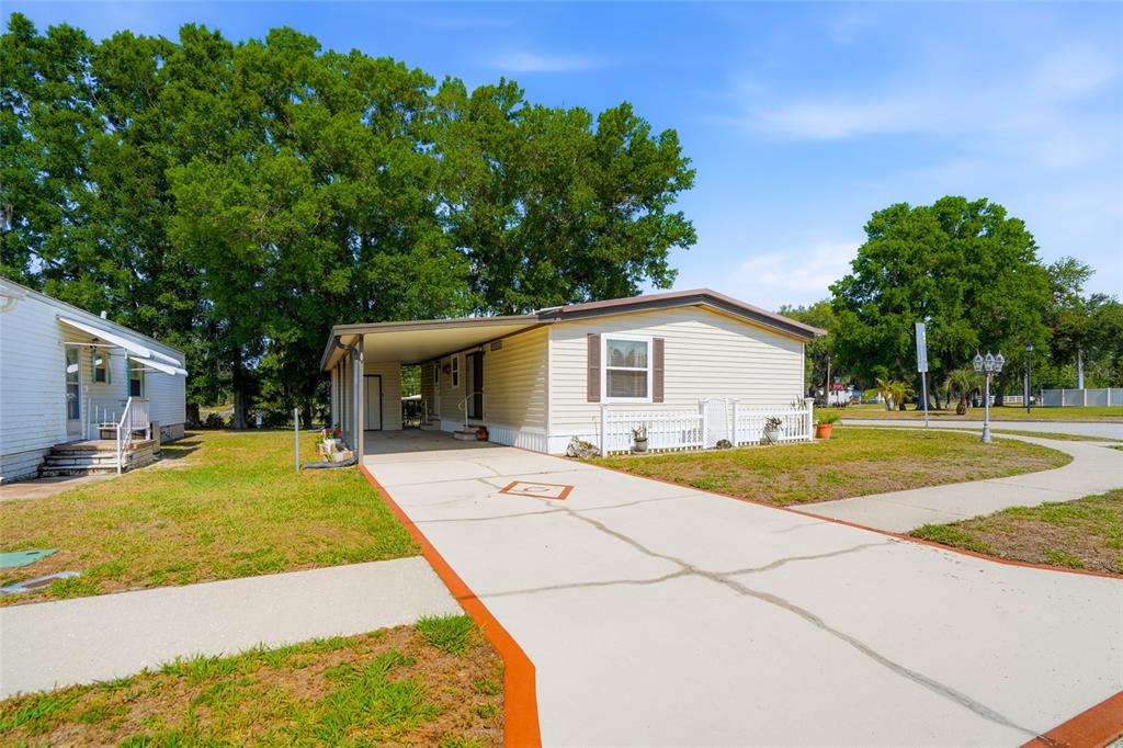 A single-story manufactured home with a carport and a concrete driveway sits on a lawn — 3933 SARAH DRIVE, WESLEY CHAPEL, FL