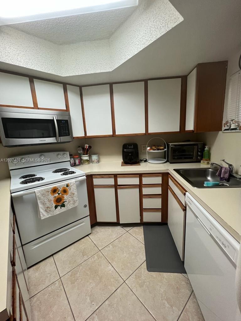 A kitchen features white cabinets with wood trim, a white stove, and a stainless microwave — 8215 Lake Dr # 401, Doral FL 33166, DORAL, FL