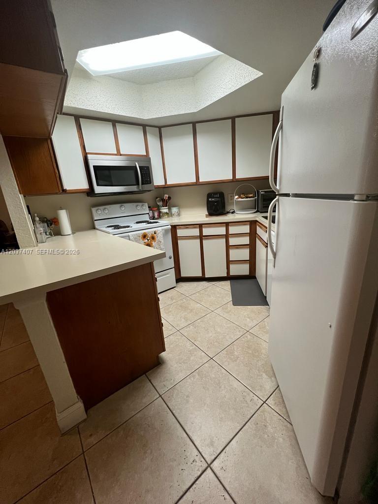 A kitchen features white cabinets, a skylight, a white stove, and a white refrigerator — 8215 Lake Dr # 401, Doral FL 33166, DORAL, FL