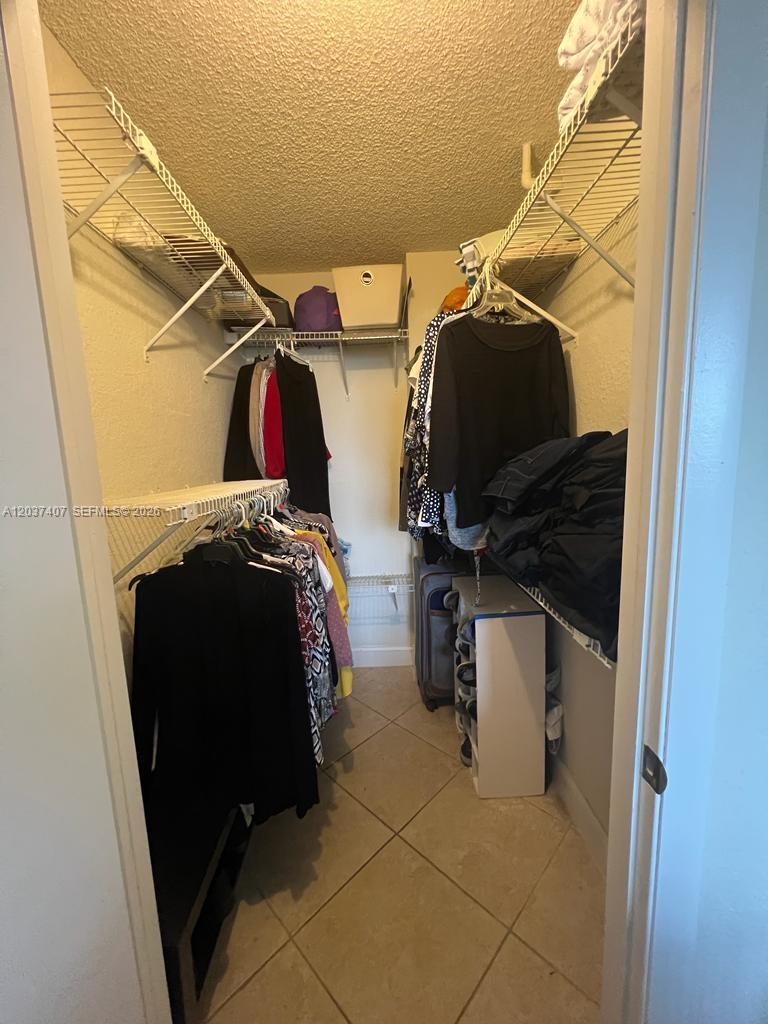 A walk-in closet features wire shelving, hanging clothes, and light-colored tile flooring — 8215 Lake Dr # 401, Doral FL 33166, DORAL, FL