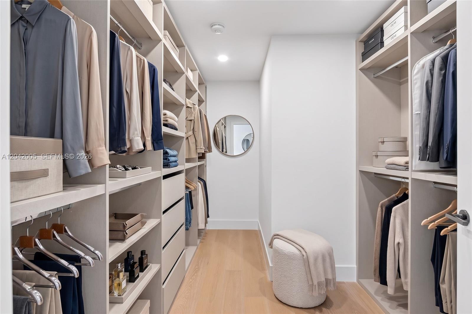 A walk-in closet features light wood flooring, built-in shelving, hanging rods, and a round mirror — 1176 97th St # 703, Bay Harbor Islands FL 33154, BAY HARBOR ISLANDS, FL