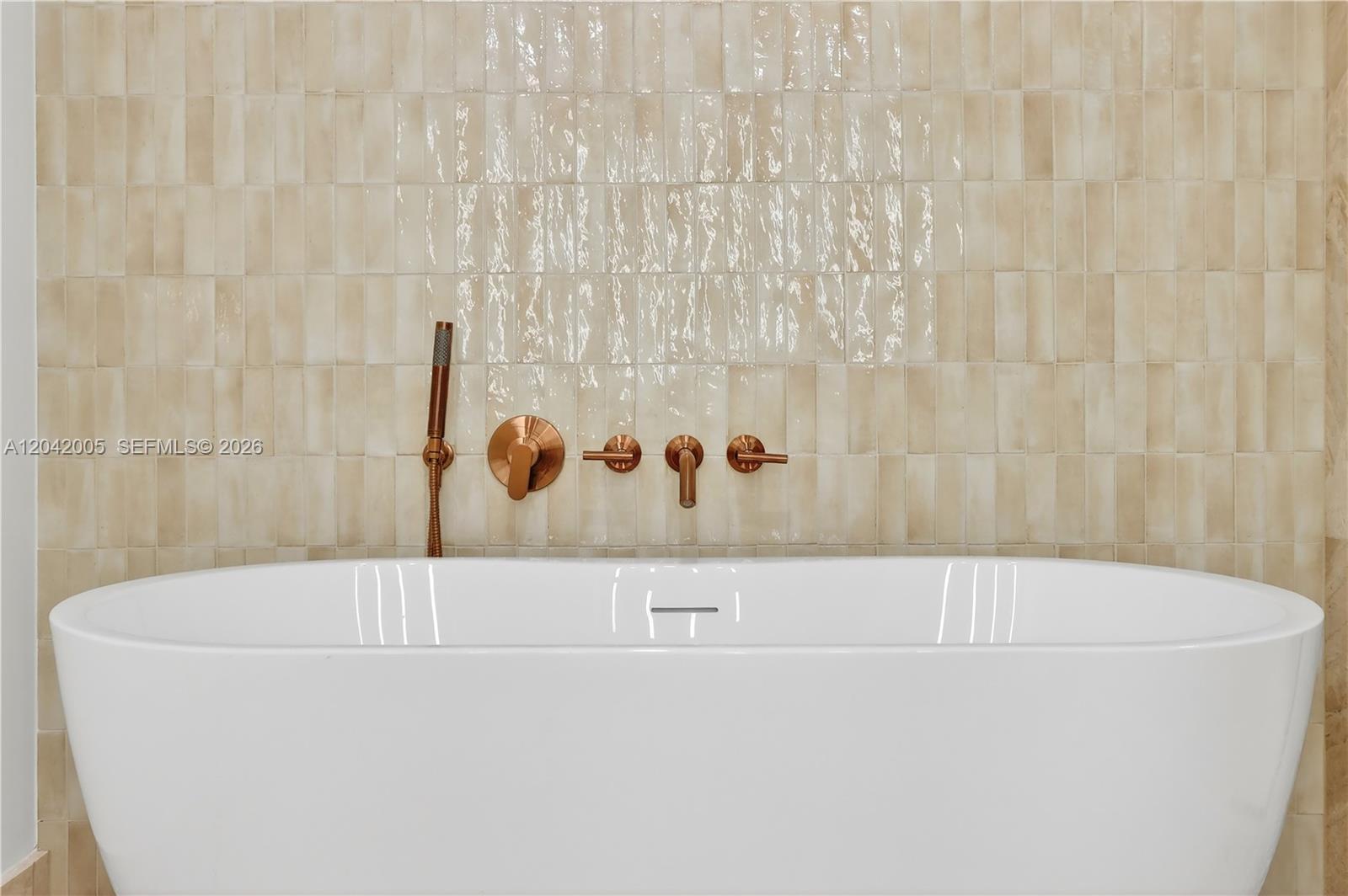 A white freestanding bathtub is positioned against a wall with glossy, light-colored vertical tiles — 1176 97th St # 703, Bay Harbor Islands FL 33154, BAY HARBOR ISLANDS, FL